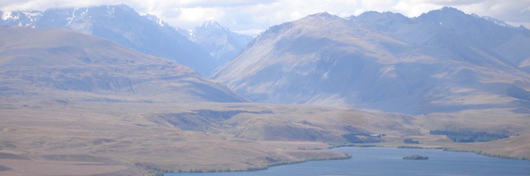 New Zealand's Lake Alexandrina backed by mountains, blue sky, and white clouds.